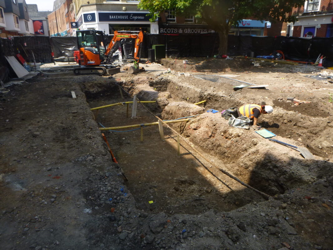 Ongoing archaeological work on St Nicolas Square with an archaeologist recording and a machine in the background.